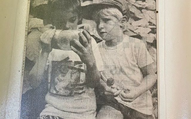 Two boys happily playing in the woods, featured in a newspaper article highlighting their adventurous spirit.