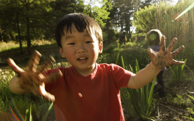 A young boy smiles while showing his muddy hands, enjoying playtime outdoors.