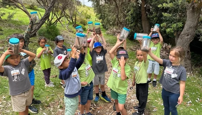 Maui school children hold up jars with soil and twigs inside.